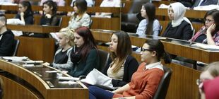 Junge Menschen sitzen als Abgeordnete in einem Parlamentsplenum und lauschen der Debatte.