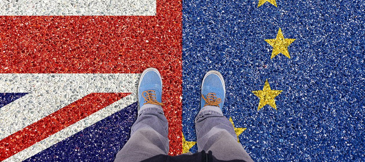 Eine Person steht mit beiden Beinen auf jeweils eine halben EU- und UK-Fahne.