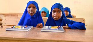 Zwei Mädchen mit Hijab sitzen auf einer Schulbank und schauen in die Kamera