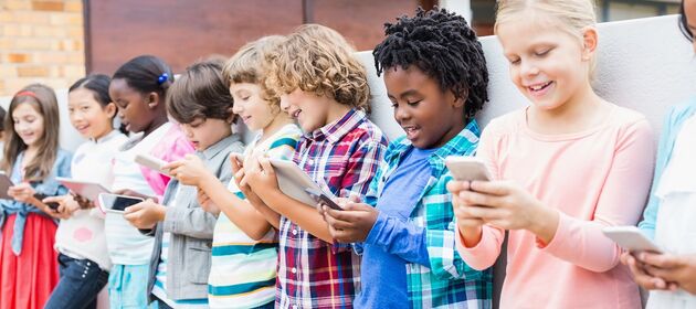 Mehrere Kinder stehen mit Smartphones und Tablets in einer Reihe