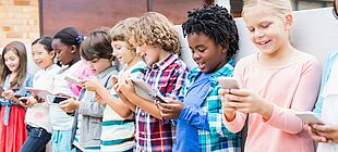 Mehrere Kinder stehen mit Smartphones und Tablets in einer Reihe
