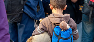 Junge in Gruppe Flüchtinge mit Rucksack aus dem ein Teddy guckt