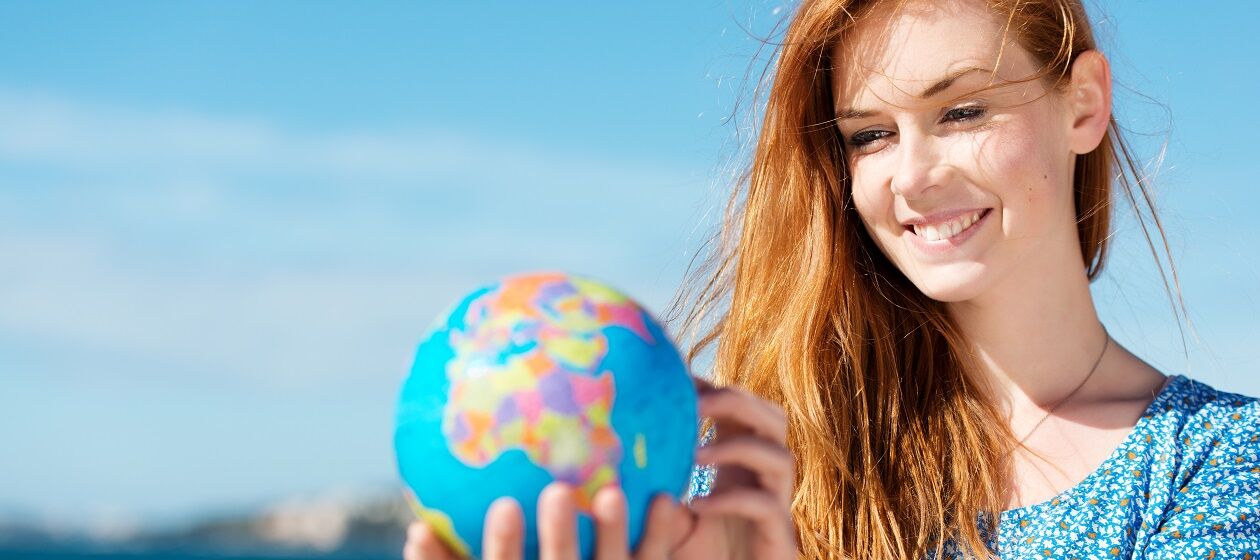 Eine junge Frau hält einen kleinen Globus in der Hand und betrachtet diesen.