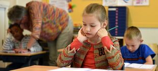 Grundschulkinder sitzen im Klassenraum und bearbeiten Aufgaben