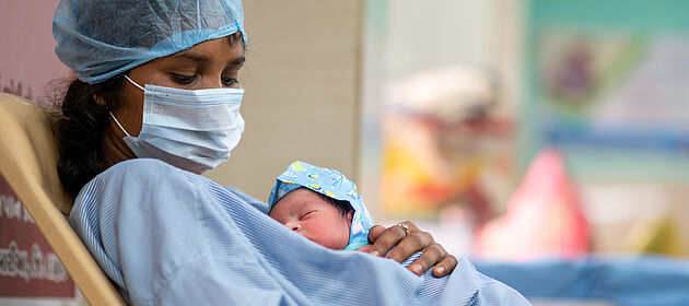 Eine Frau mit Mundnasenschutz hält ein neugeborenes Baby auf dem Arm