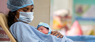 Eine Frau mit Mundnasenschutz hält ein neugeborenes Baby auf dem Arm