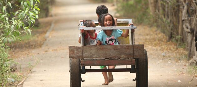 Mehrere Kinder sitzen auf einem selbstgebauten Wagen, der von einer Person gezogen wird