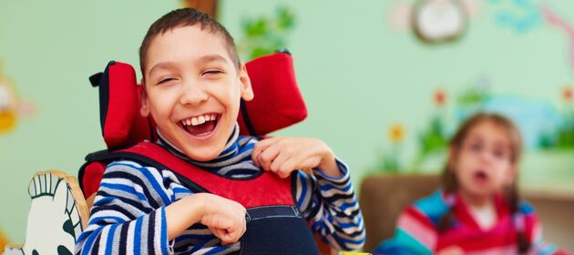 Junge mit Beeinträchtigung im Rollstuhl lacht glücklich in die Kamera