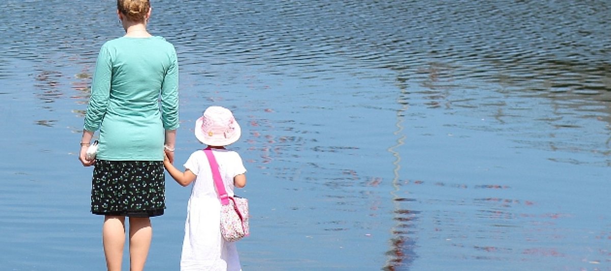 eine Frau steht mit einem Kind am See und blickt auf das Wasser