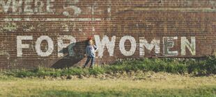 Ein Mädchen steht vor einer Mauer auf der mit weißer Farbe "FOR WOMEN" steht
