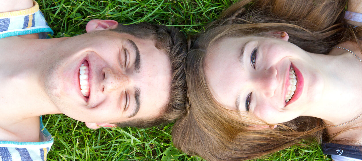 Zwei Jugendliche liegen lächelnd im Gras
