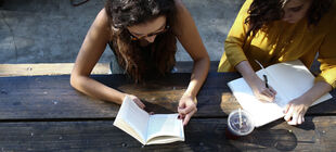 Zwei junge Frauen sitzen an einem Holztisch und schreiben etwas auf
