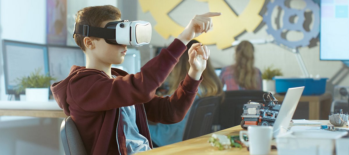 Ein Teeanager sitzt im Technikraum der Schule und schaut in eine Virtual Realtiy Brille.