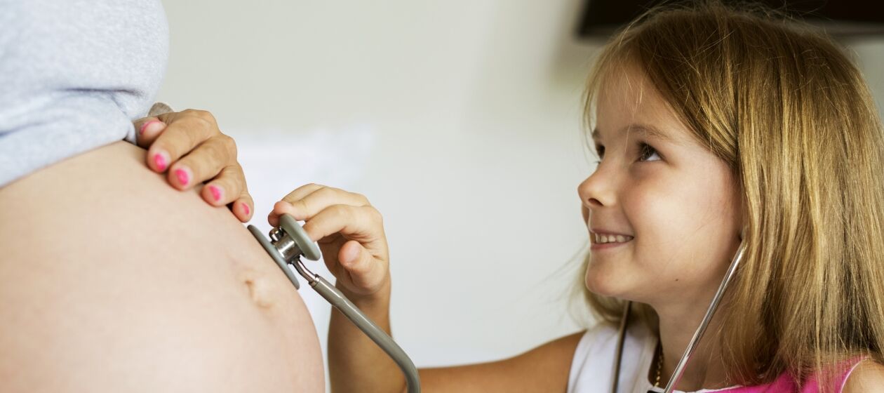 Kleines Mädchen legt freudig ein Stetoskop auf einen Schwangerenbauch