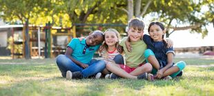 Eine Gruppe Kinder sitzt Arm in Arm auf einer Wiese und lacht in die Kamera
