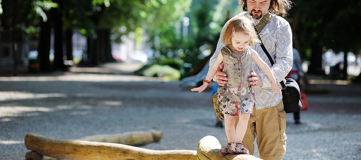 Mann hilft kleinem Mädchen beim Balancieren auf einem Baumstamm