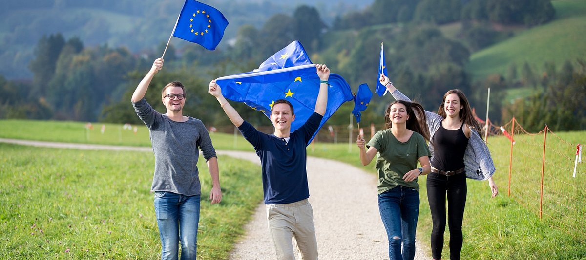Vier Jugendliche im ländlichen Raum, die begeistert Europaflaggen schwenken