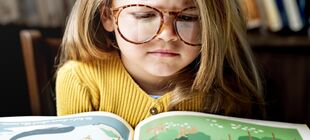 Ein Mädchen mit einer großen Brille schaut konzentriert in ein Kinderbuch
