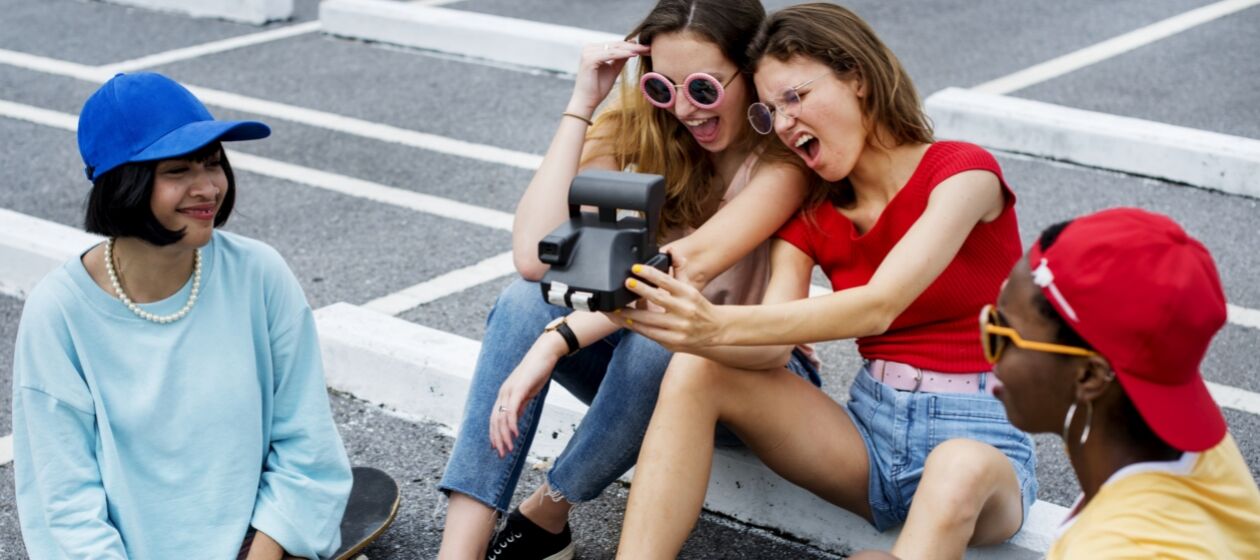 Vier Jugendliche sitzen auf einem Parkplatz und machen Fotos mit einer Polaroidkamera