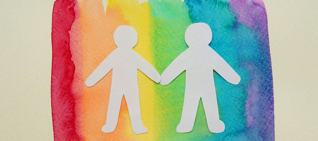 Zwei Papiermännchen auf einer Regenbogenfahne halten sich an den Händen.