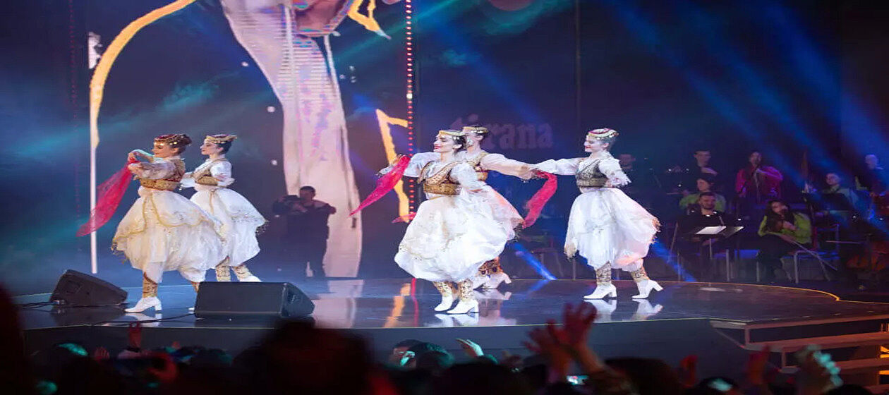 Auf dem Bild sind Tänzerinnen in traditionellen Albanischen Kleidern zu sehen, die auf einer Bühne tanzen.