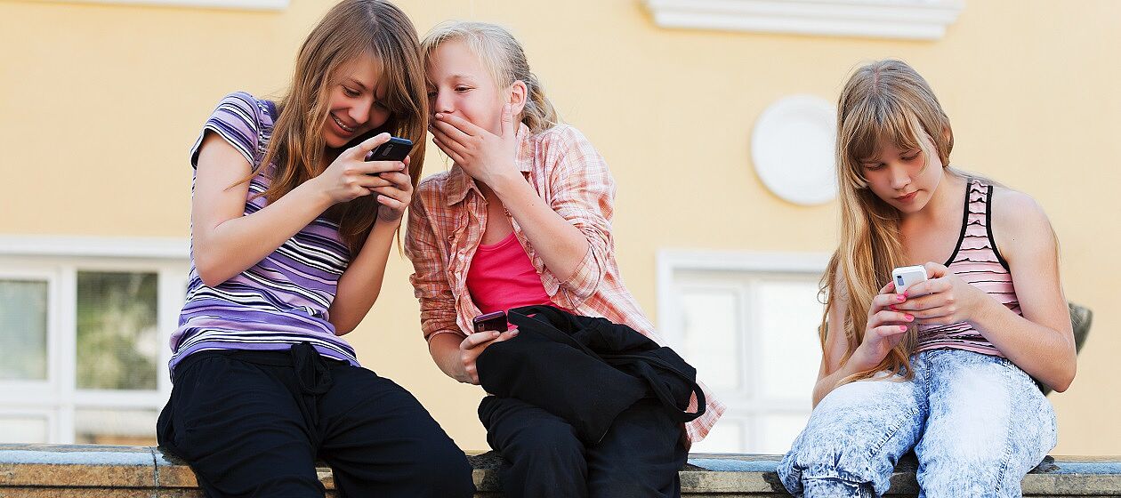 3 Mädchen sitzen mit ihren Handys auf der Mauer