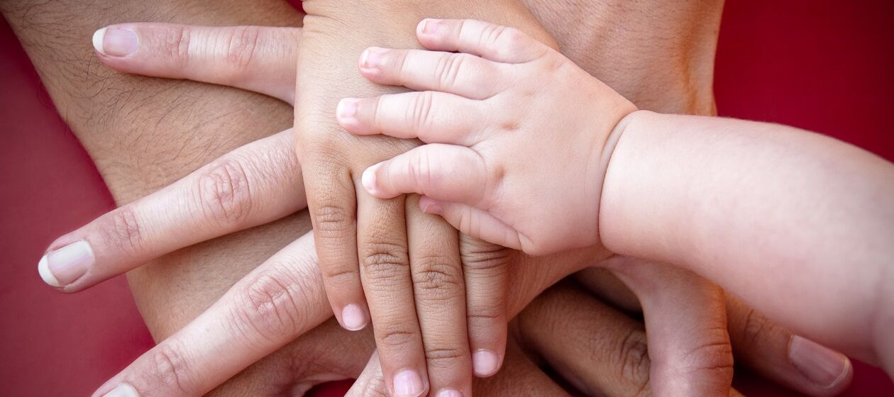 Mutter, Vater, Kind und Baby legen ihre Hände aufeinander.