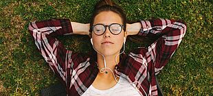 Eine jugendliche Person liegt mit geschlossenen Augen auf dem Gras und hat Kopfhörer in den Ohren
