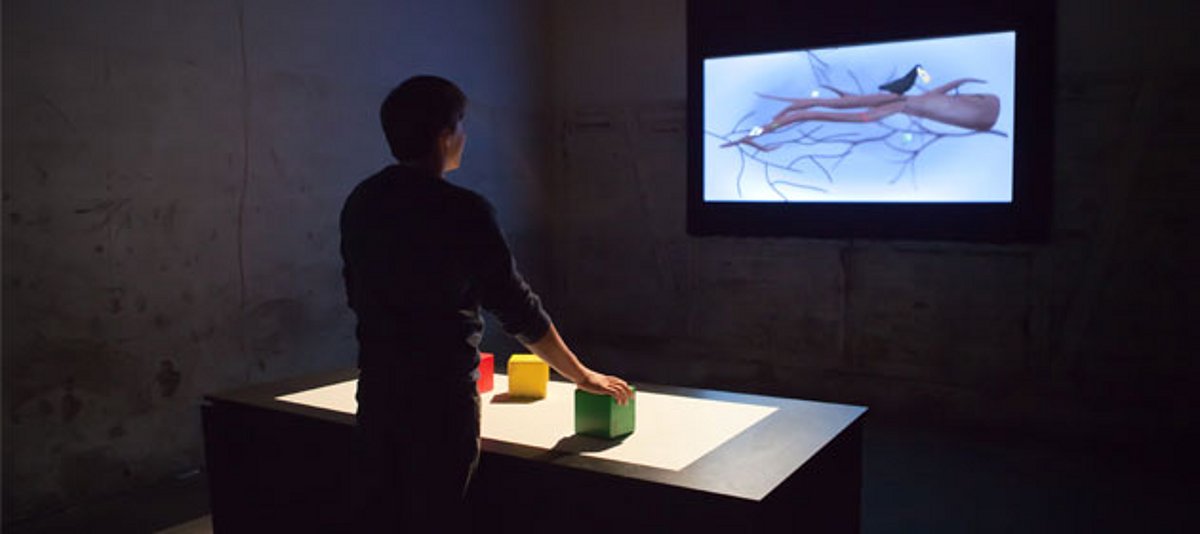 Junger Mann dirigiert mit drei bunten Würfeln auf dem Tisch virtuelle Figur im Computer (Geek Run)