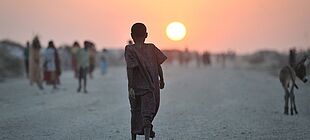 Ein Mädchen läuft mit dem Rücken zur Kamera in den Sonnenaufgang