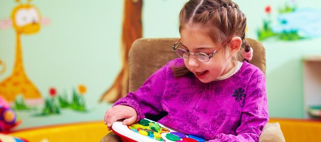 Ein fröhliches Mädchen mit dicken Brillengläsern ist intensiv mit einem Spielzeug beschäftigt.