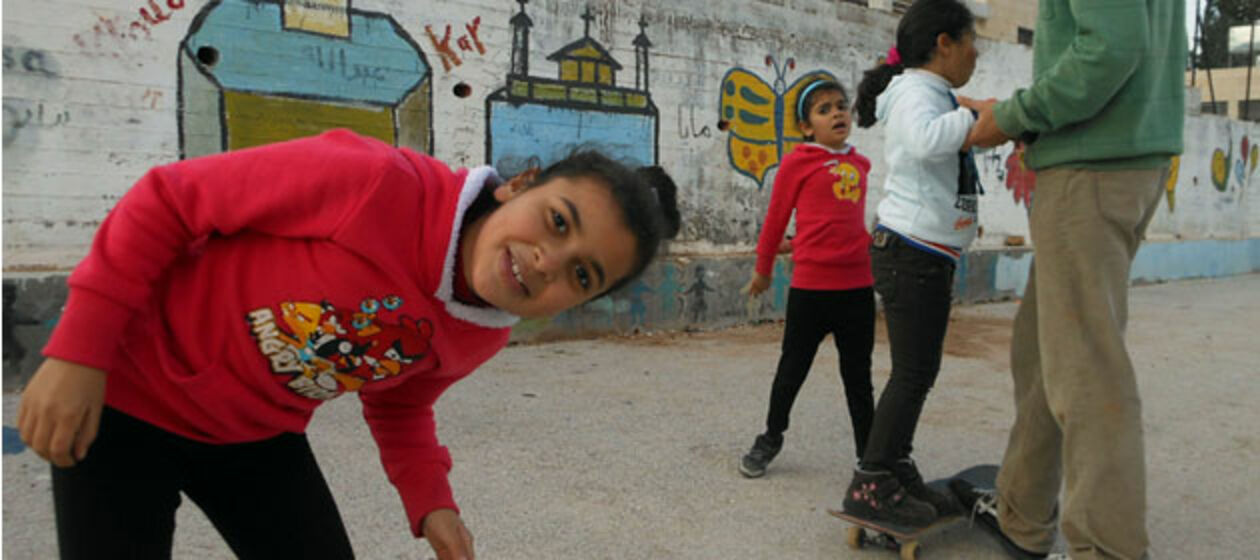 Kinder und Freiwilliger mit Skateboard vor Grafitti-Wand