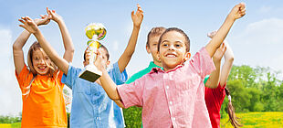 Frühliche Kinder halten einen Pokal in die Höhe.