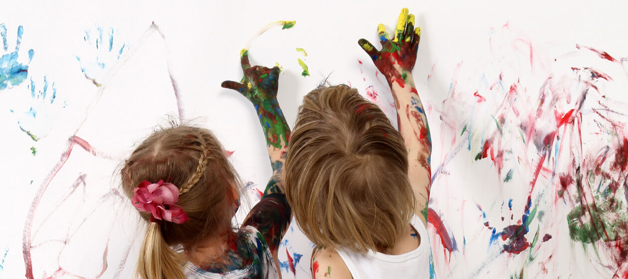 Zwei Kinder bemalen eine Wand mit Fingerfarben