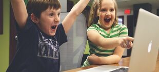 Zwei Kinder vor einem Laptop reißen begeistert Mund und und Augen auf.