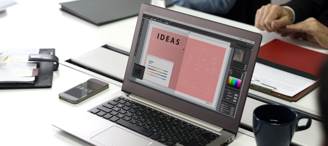 Ein Bürotisch auf dem eine Tasse, ein Smartphone und ein Laptop stehen, auf dessen Bildschirm das Wort Ideas zu lesen ist