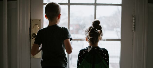 Ein Junge und ein kleineres Mädchen sind zuhause und schauen durch eine Glastür nach draußen