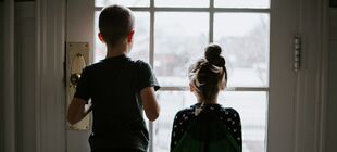 Ein Junge und ein kleineres Mädchen sind zuhause und schauen durch eine Glastür nach draußen