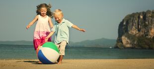 Zwei Kinder spielen am Strand ausgelassen mit einem Ball 