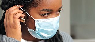 Eine junge Frau zieht eine Mund-Nase-Bedeckung auf