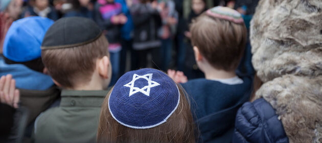 Jüdische Kinder zum Teil mit Kippa stehen in einer Gruppe zusammen und schauen beim Verlegen von Stolpersteinen zu.