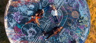 Vier Jugendliche liegen unter freiem Himmel auf dem Rücken auf einer mit Graffitti versehenen Fläche