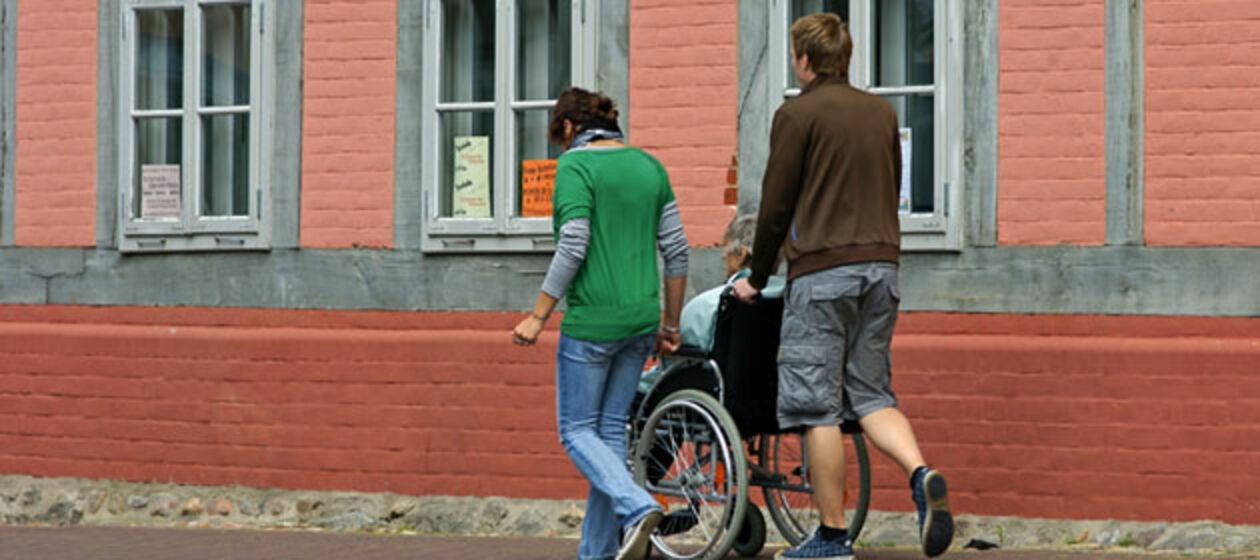 Ein junger Mann und eine junge Frau schieben einen Rollstuhl