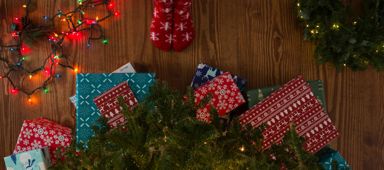 Geschenke liegen vor einem Weihachtsbaum, vor dem jemand mit roten Socken steht.