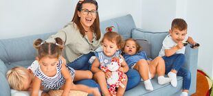Eine Frau sitzt mit fünf Kindern auf einem Sofa