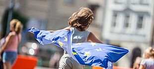 Ein Kind rennt mit einer wehenden Europaflagge hinter sich
