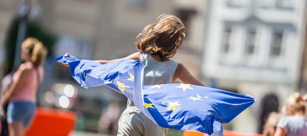 Ein Kind rennt mit einer wehenden Europaflagge hinter sich