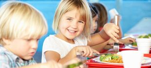 Mehrere Kinder essen gemeinsam zu Mittag, das Mädchen in der Mitte lächelt