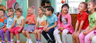 Eine Gruppe Kinder sitzt auf einer Bank im Kindergarten. Alle lachen.