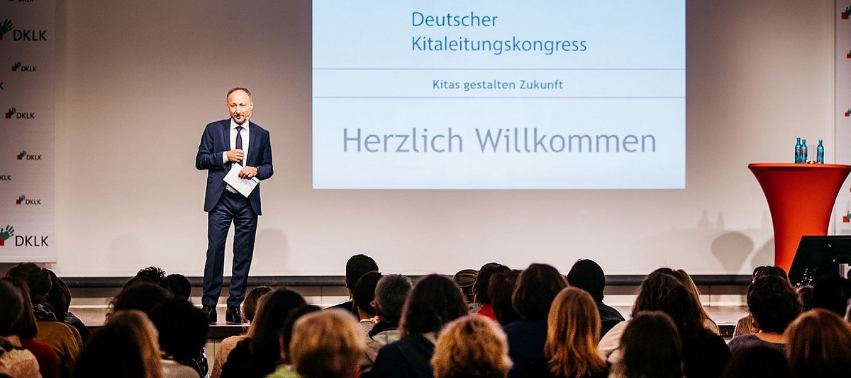 Moderator eröffnet auf einer Bühne den Deutschen Kitaleitungskongress